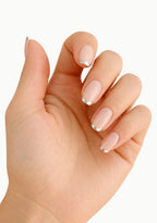 A close-up of a hand with a French manicure, showcasing a glossy pale pink base and a sharp metallic silver tip on each nail, set against a plain white background.